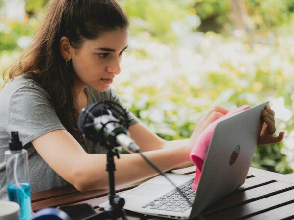 Young female vlogger with mic and dumbbells holding a cloth and spray bottle to clean laptop