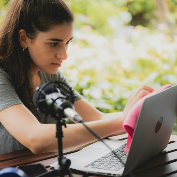 Young female vlogger with mic and dumbbells holding a cloth and spray bottle to clean laptop