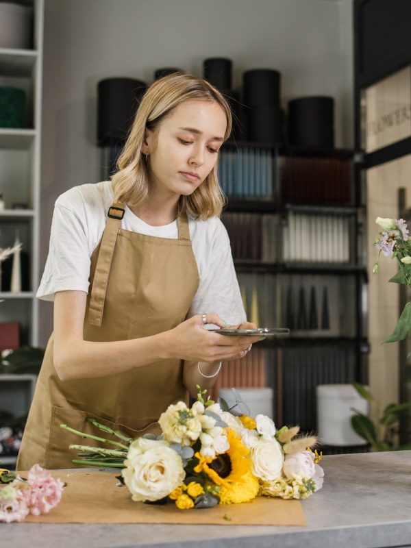 Caucasian woman taking photo of finished flowers bouquet for social media. Floristry concept.